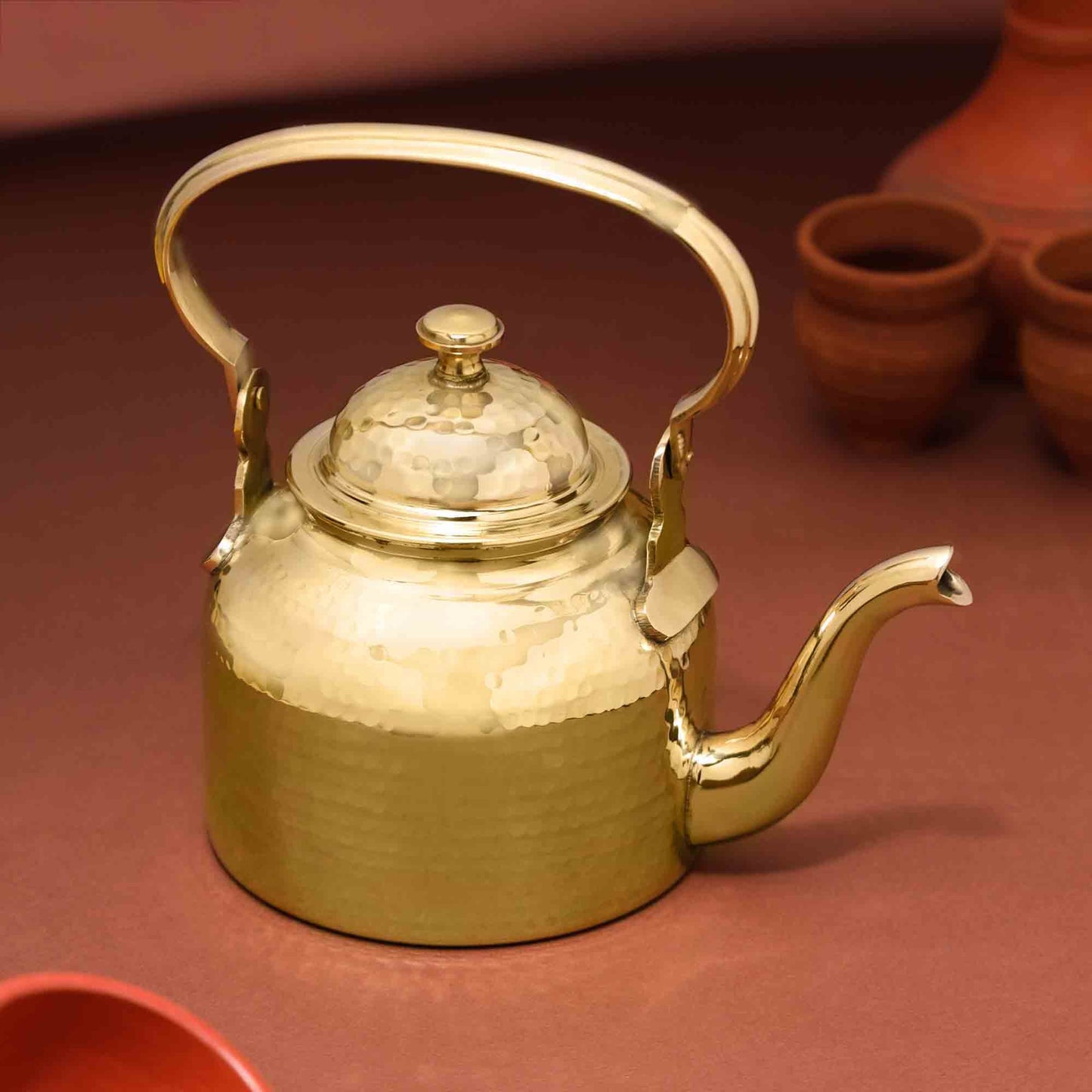 Gold teapot on a brown surface with terracotta pots in the background