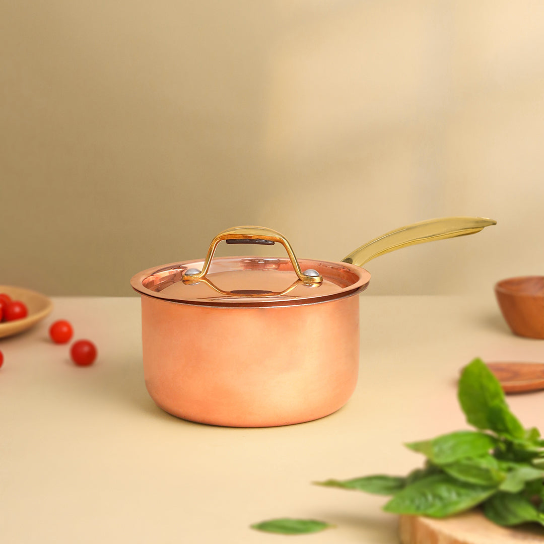 Copper pot with a lid on a light surface with greenery and small items.