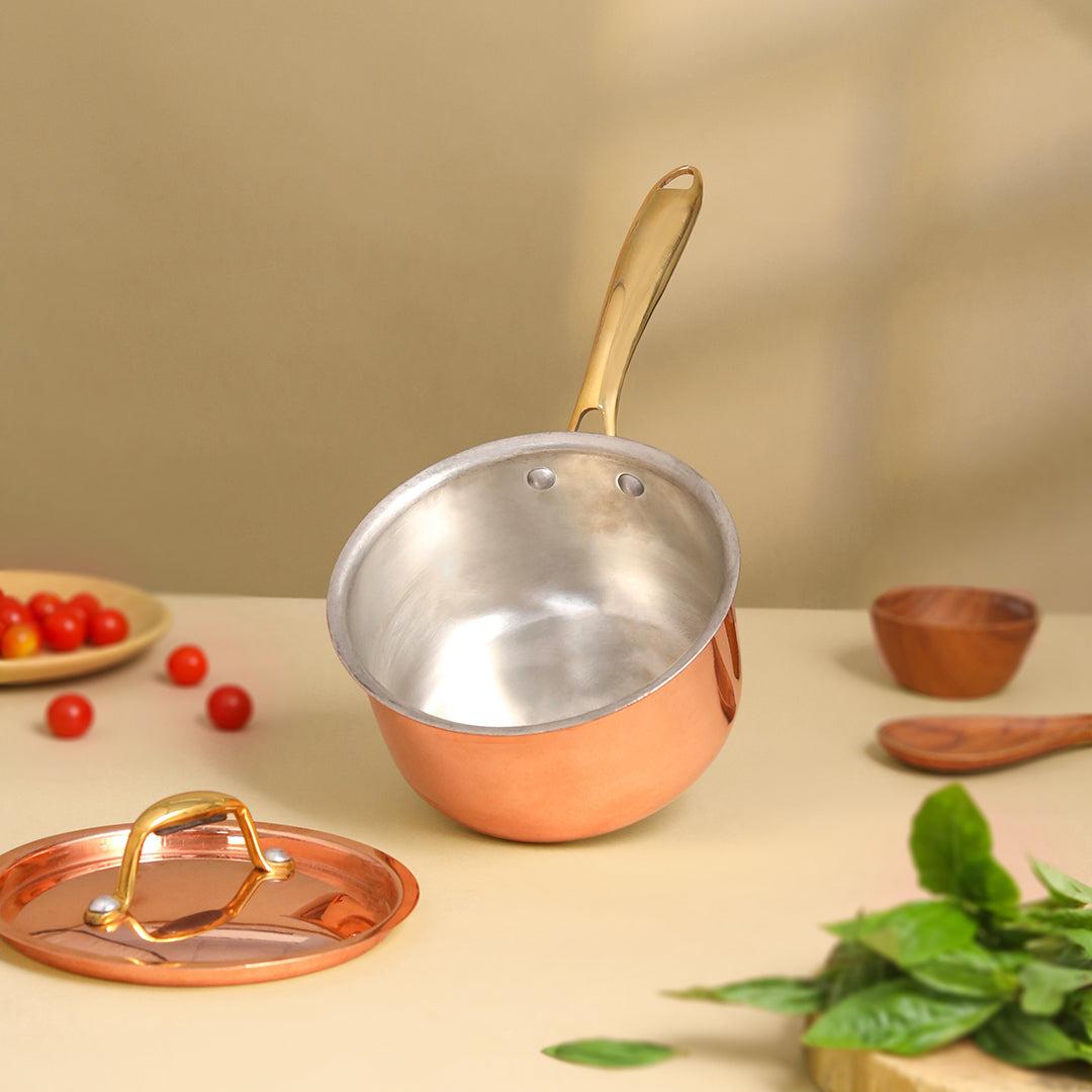 Copper saucepan with a lid on a table with vegetables and a wooden bowl.