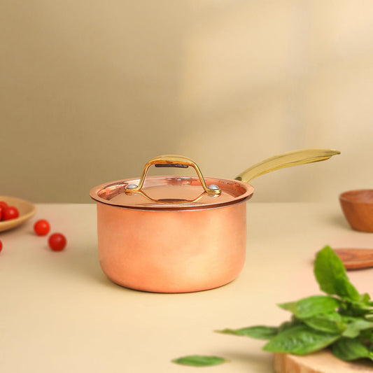 Copper pot with a lid on a light surface with greenery and small items.