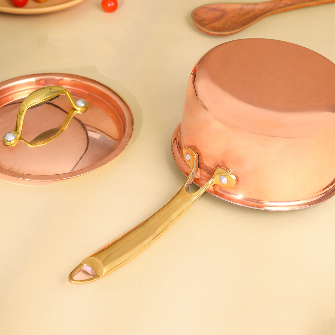 Copper saucepan with gold handle on a beige background